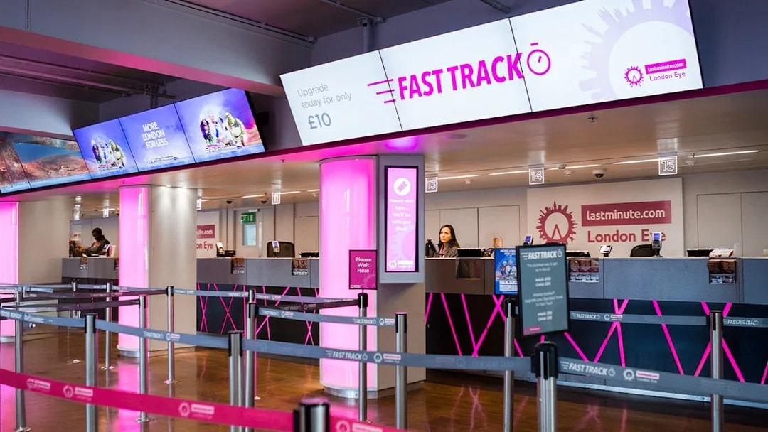 Fast track ticket counter for the London Eye with pink signage and queue barriers.