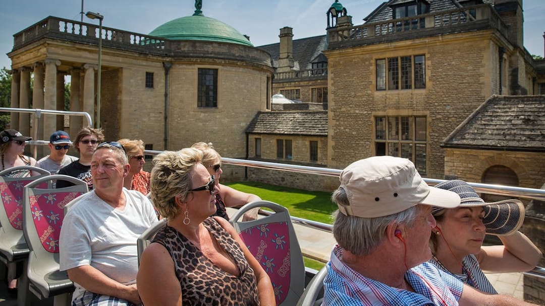 Tourists on an open-top bus tour in Oxford, viewing historic architecture.