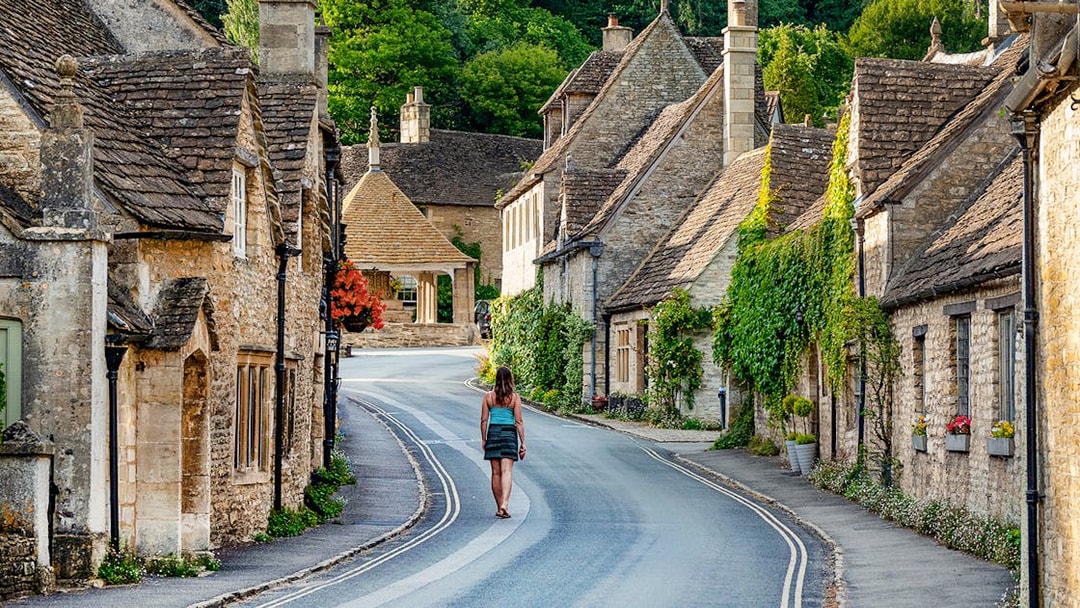 Cotswolds village street with stone cottages and a person walking, Oxford tour.