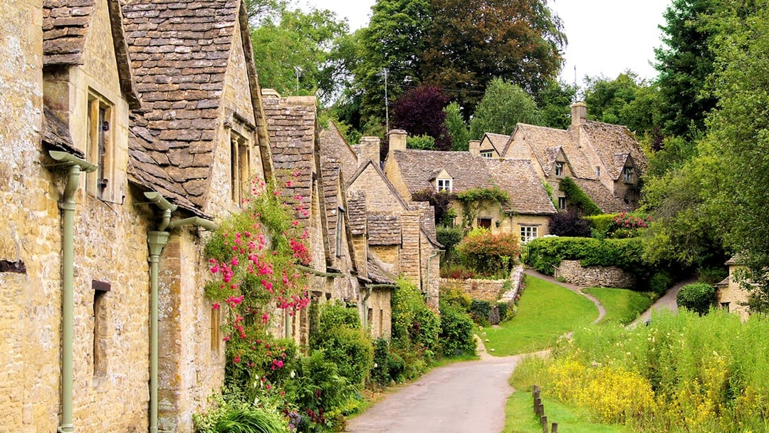 Arlington Row cottages in Bibury, Cotswolds, with stone walls and lush greenery.