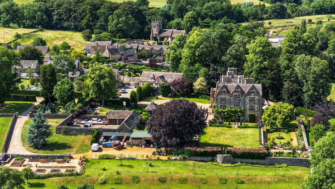 Aerial view of a Cotswolds village with historic stone buildings and lush gardens, Oxford tour.