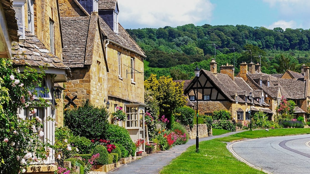 Cotswolds village street with stone cottages and lush gardens.