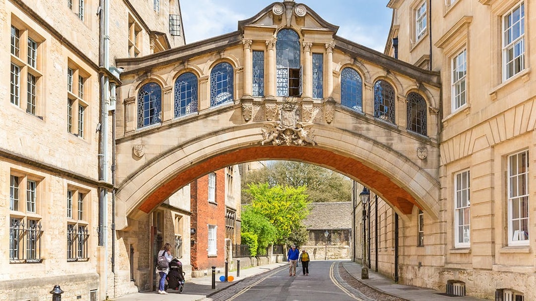 Bridge of Sighs over a street in Oxford, England, with pedestrians walking below.