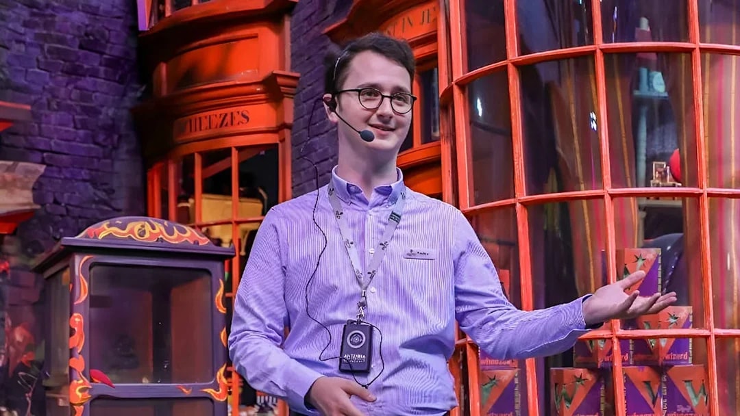 English-speaking guide presenting at a themed attraction with colorful storefronts.