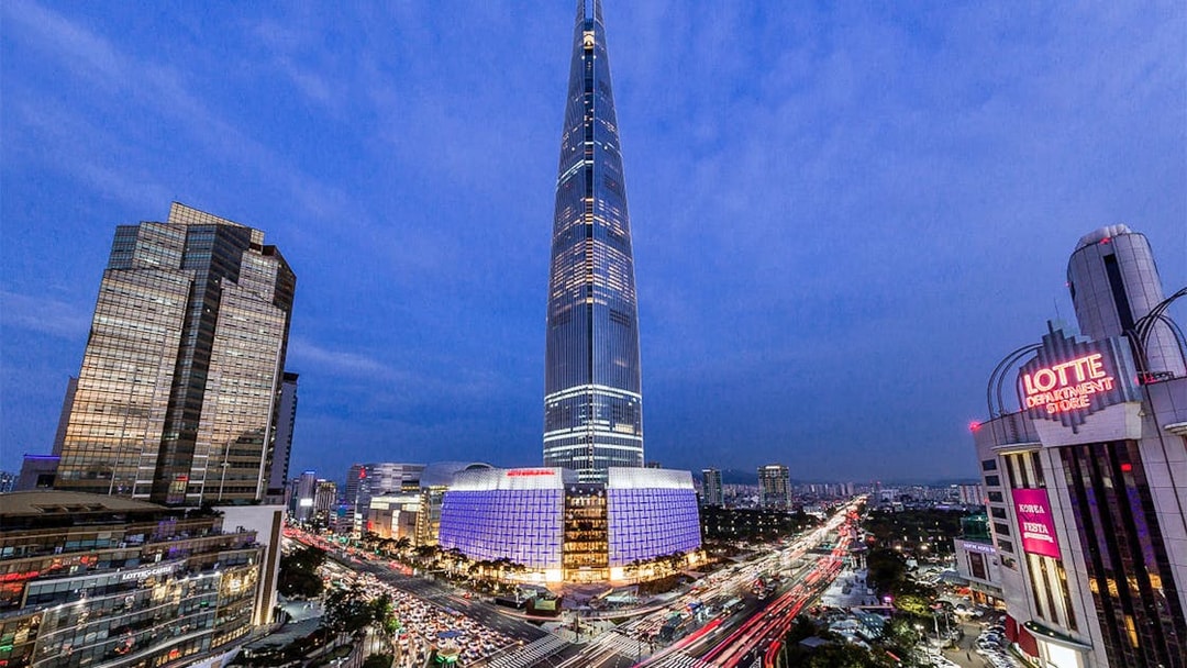 Lotte World Tower illuminated at night in Seoul, with cityscape and traffic below.