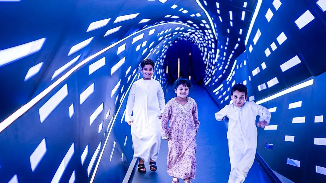 Children walking through an illuminated tunnel at Louvre Abu Dhabi.