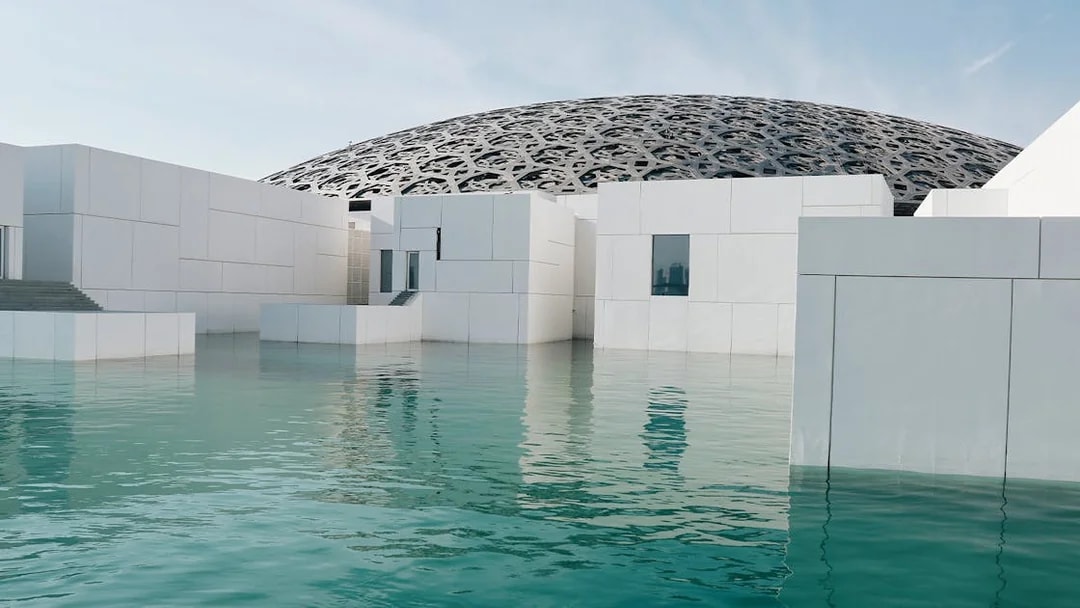 Louvre Abu Dhabi exterior with water reflection and dome structure.