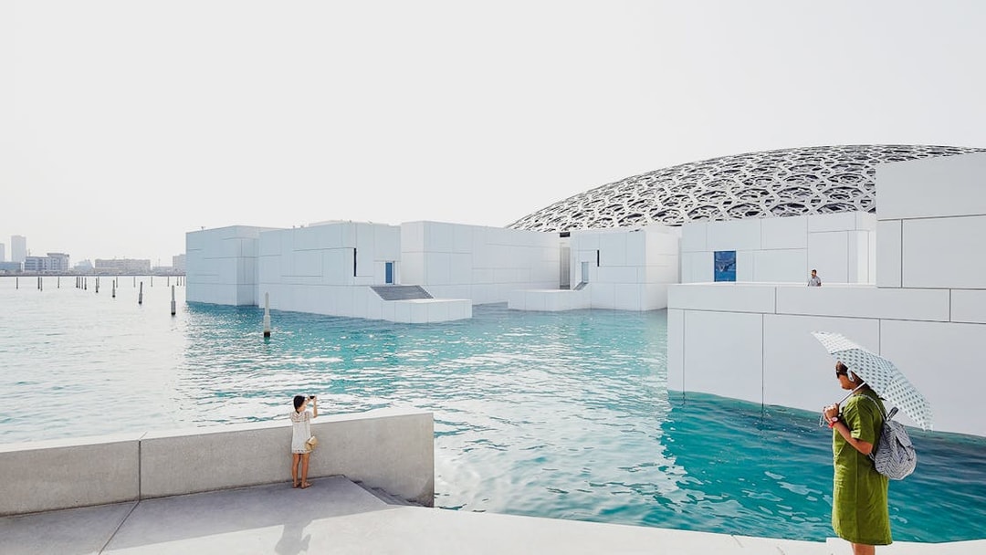 Louvre Museum Abu Dhabi with dome and water, visitors exploring the exterior.