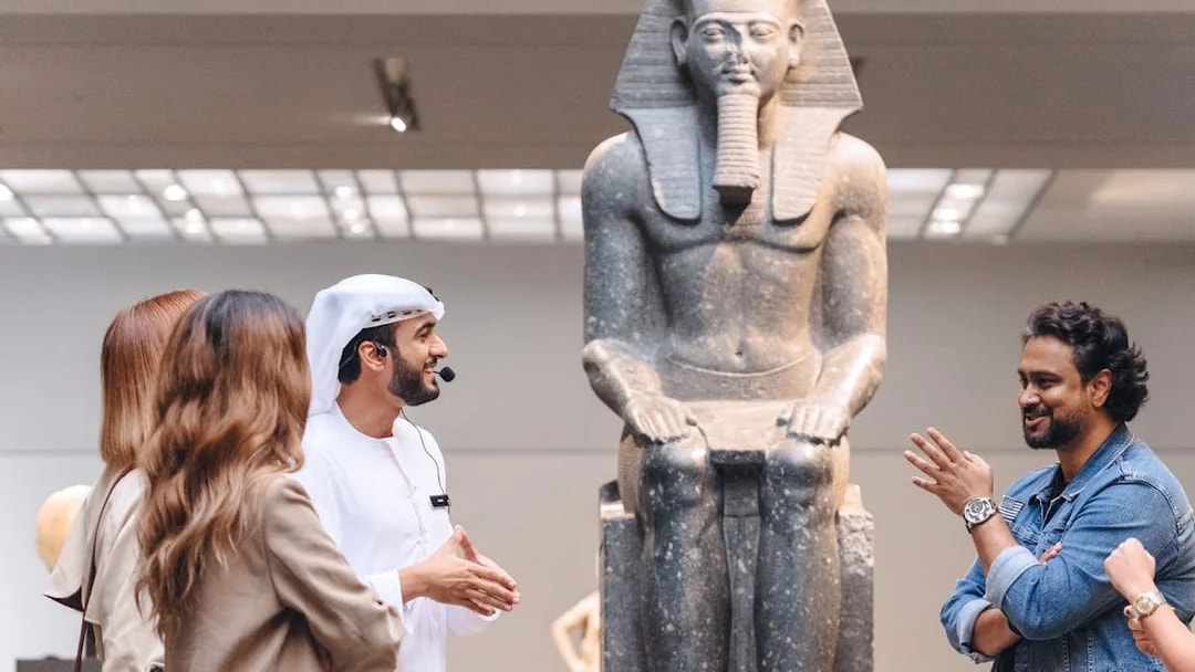 Guests engaging with a guide near an ancient statue at Louvre Museum Abu Dhabi.