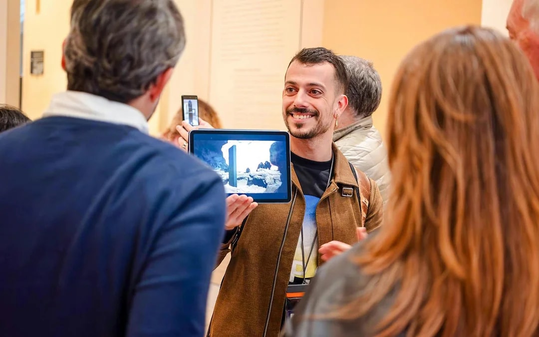 Guide showing tablet to tourists inside Louvre Museum, France.