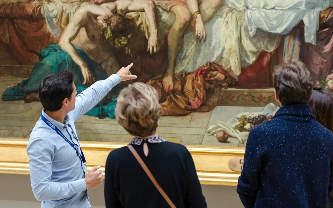 Guide explaining painting to tourists inside Orsay Museum, France.