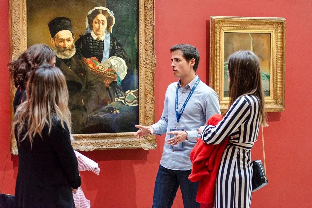 Guide explaining paintings to tourists inside Orsay Museum, France.
