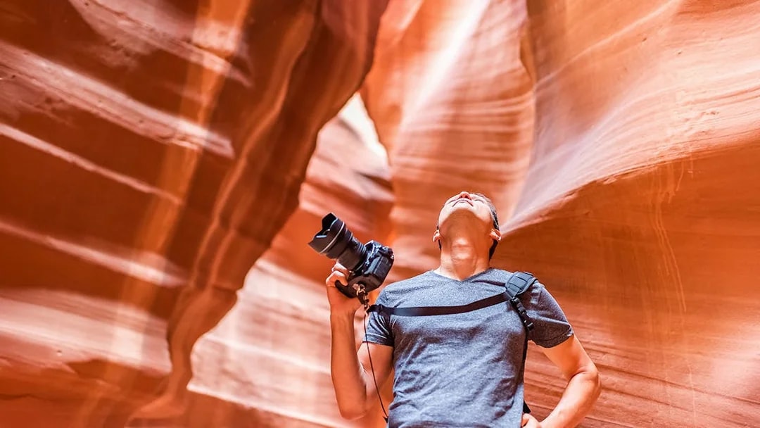 Tourist with camera exploring Lower Antelope Canyon's narrow pathways in Arizona.