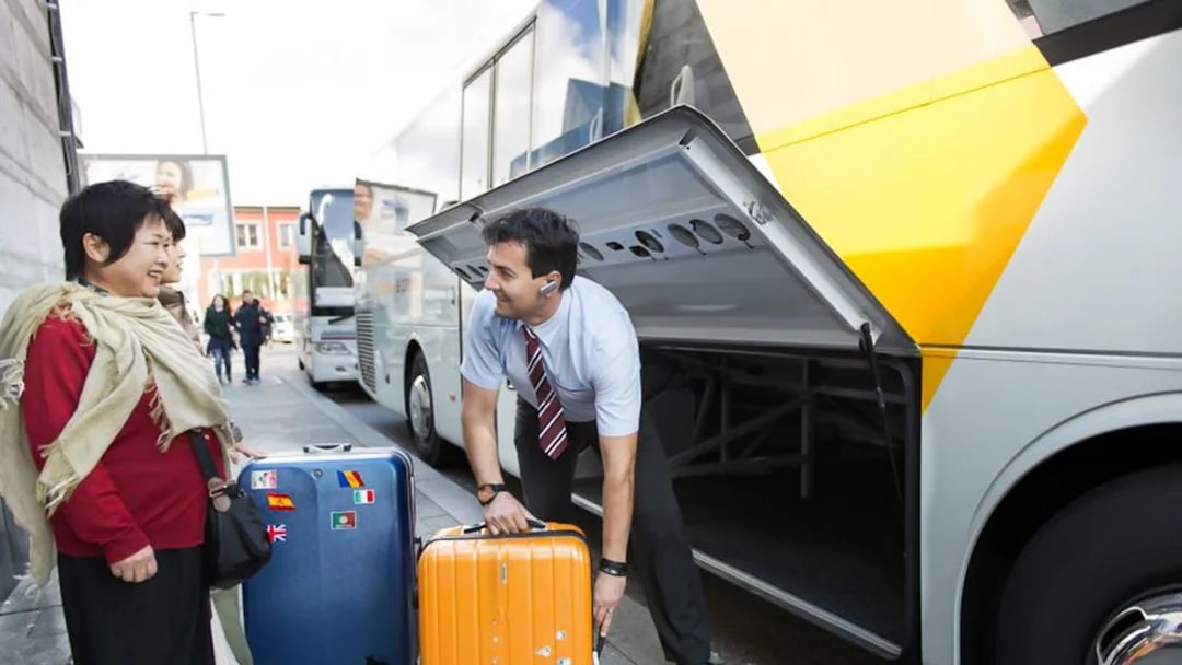 Staff assisting passenger with luggage at a bus terminal.