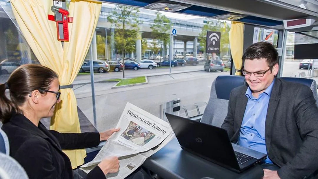 Passenger reading newspaper on airport transfer bus with free WiFi.