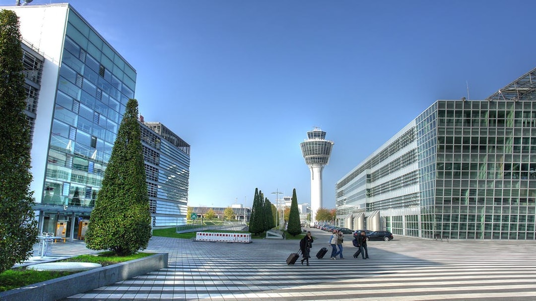 Munich Airport terminal with control tower and travelers walking with luggage.