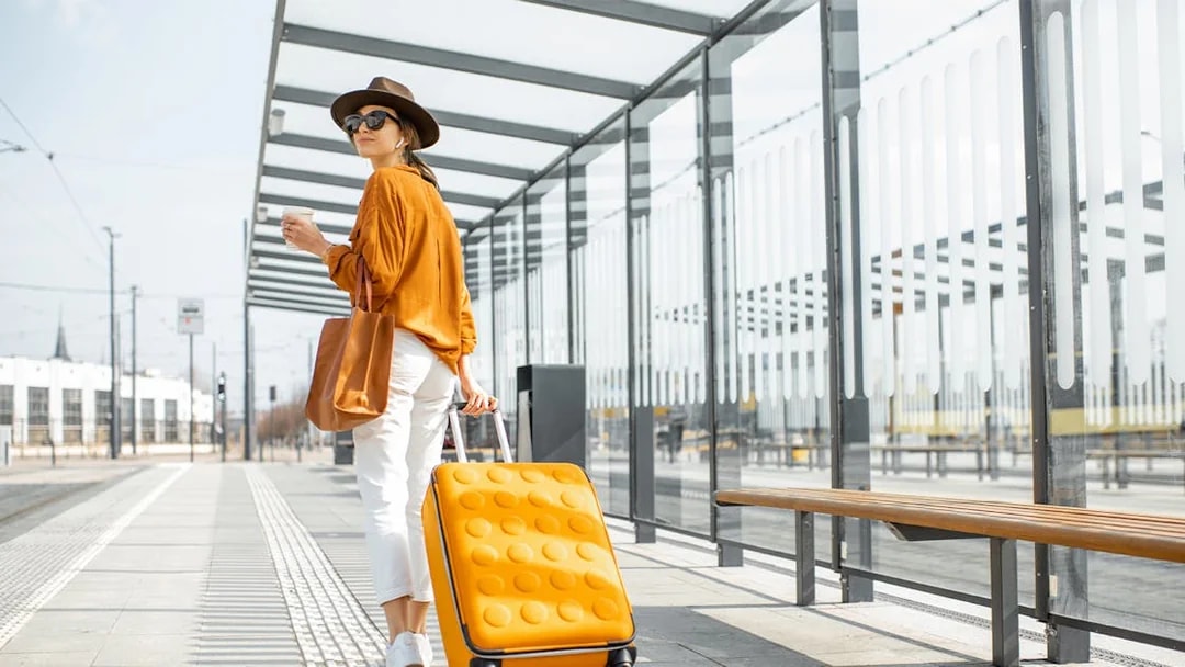 Young female traveler with orange luggage at a modern tram station.