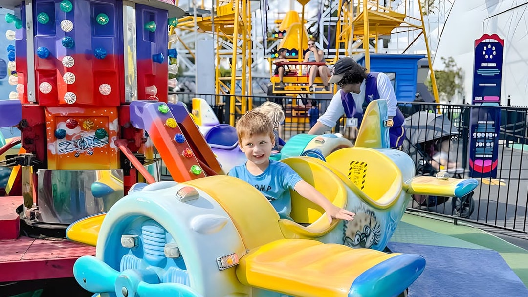Child smiling on a colorful airplane ride at Luna Park.