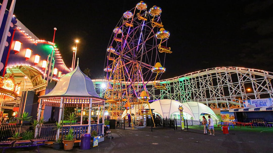 Ferris wheel illuminated at night in Luna Park, Melbourne, with roller coaster in background.