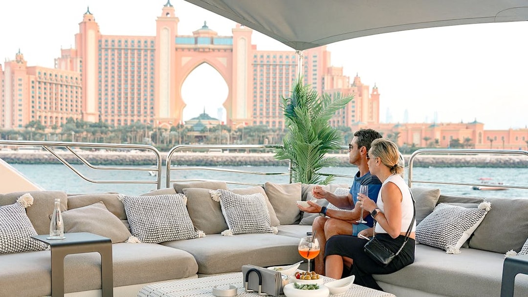 Couple enjoying gourmet dining on a yacht with Atlantis, The Palm in Dubai in the background.