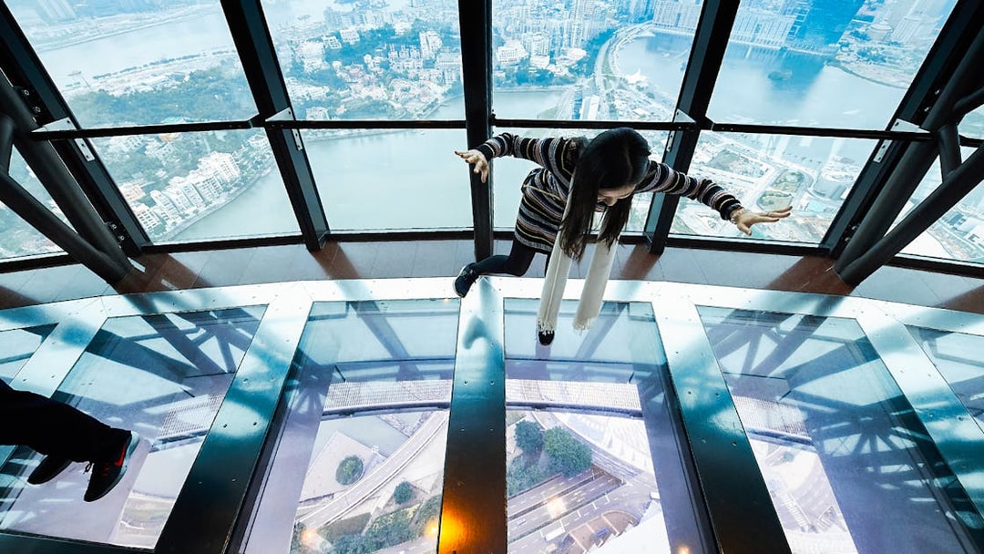Person walking on glass floor at Macau Tower with city view below.