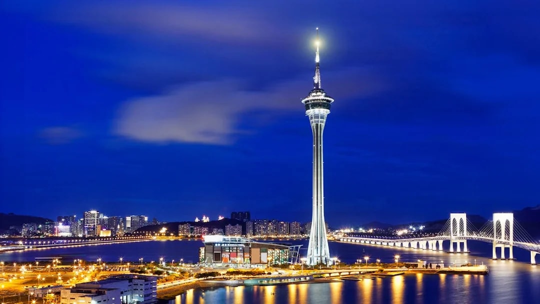 Macau Tower illuminated at night with city skyline and bridge in the background.