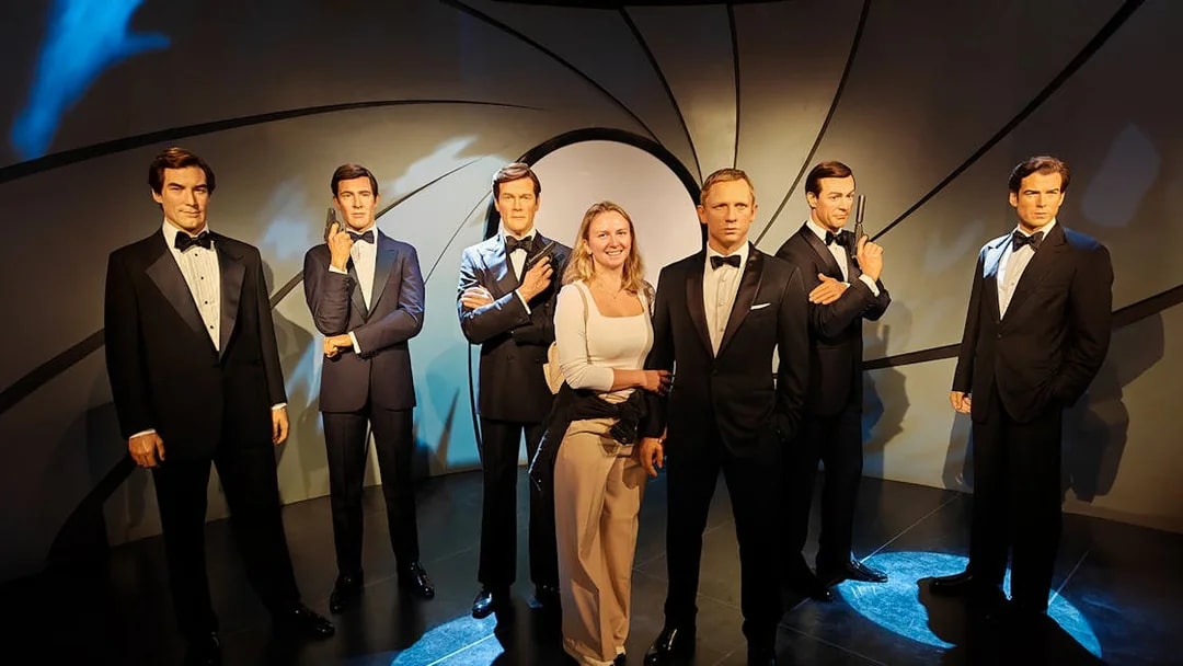 Wax figures of James Bond actors at Madame Tussauds with a visitor.