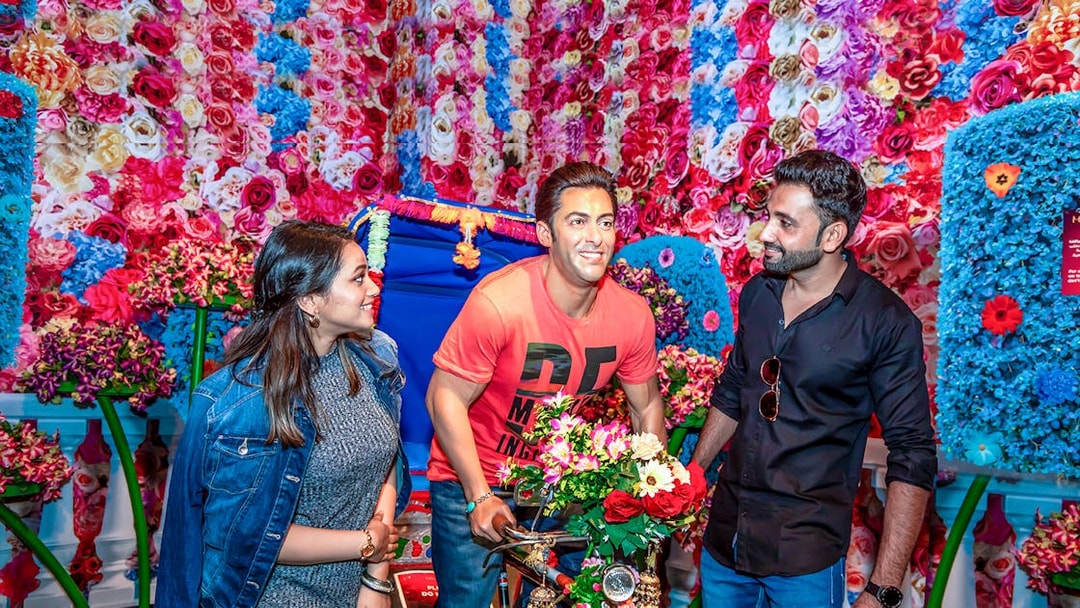 Visitors interacting with a wax figure at Dubai Madame Tussauds, surrounded by colorful flowers.