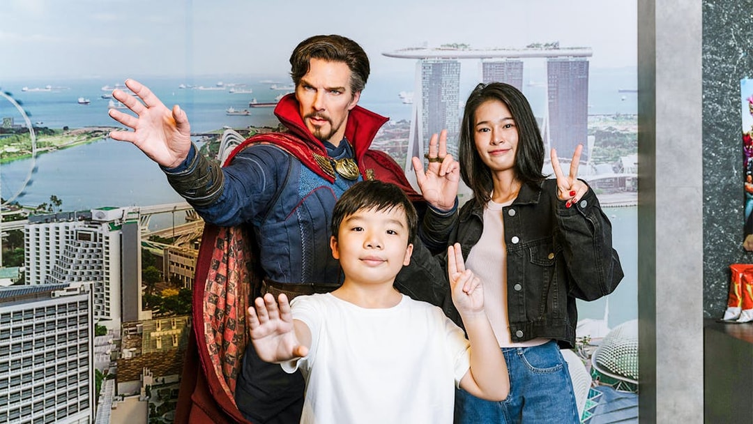 Wax figure of a superhero with visitors at Madame Tussauds Singapore, Marina Bay Sands backdrop.