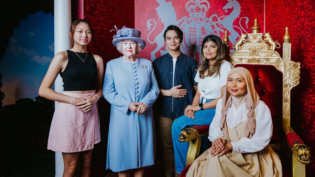 Visitors posing with a wax figure of the queen at Madame Tussauds Singapore.
