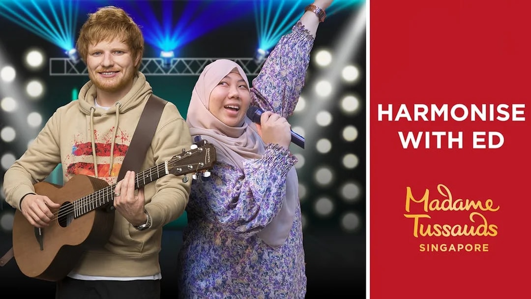 Wax figure of a musician with a guitar and a visitor singing at Madame Tussauds Singapore.