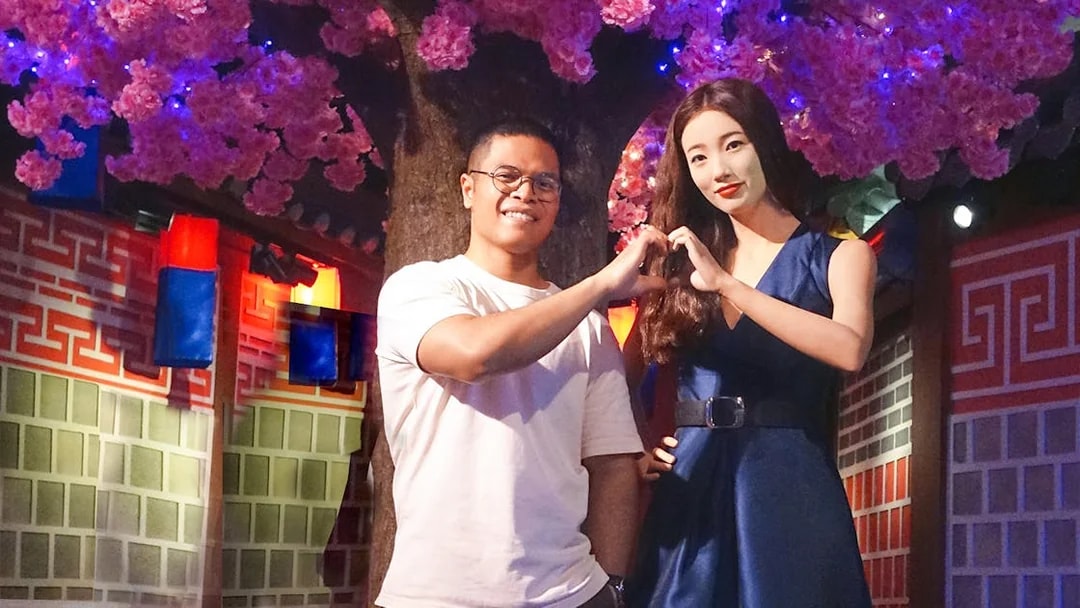 Man posing with wax figure at Madame Tussauds Singapore under cherry blossoms.