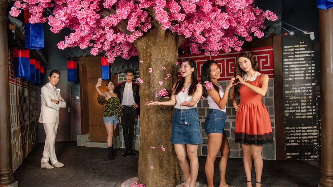 Wax figures of film stars with visitors at Madame Tussauds Singapore under cherry blossoms.