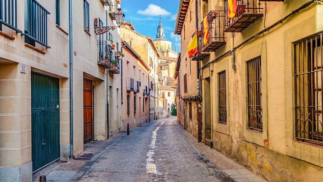 Cobbled medieval street in Segovia with Spanish flags and historic buildings.