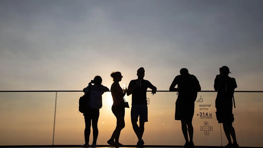 Silhouettes of people enjoying sunset views at Mahanakhon SkyWalk, Bangkok.