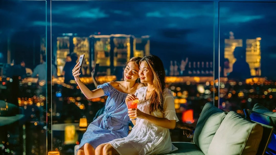 Friends taking a selfie on Mahanakhon SkyWalk, Bangkok, Thailand at night.