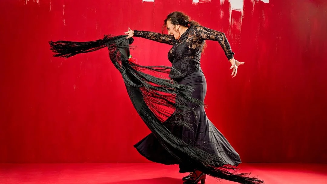 Flamenco dancer performing with a black shawl against a red background at Esencia espectáculo.