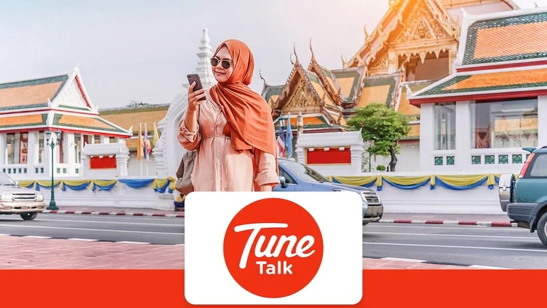 Traveler using phone with Tune Talk SIM card in front of traditional architecture in Kuala Lumpur, Malaysia.