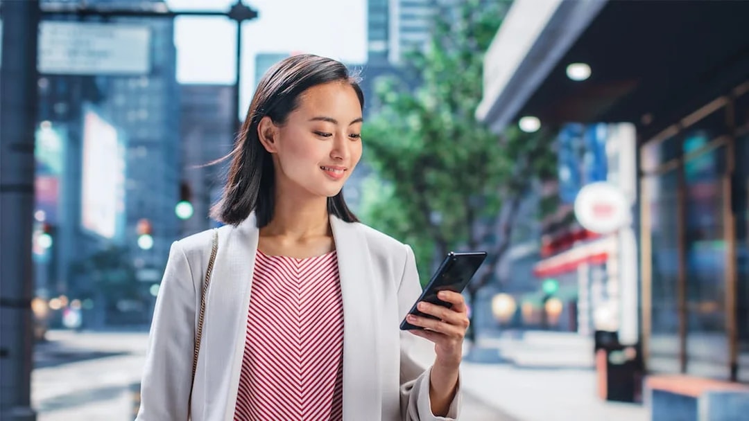 Person using smartphone on a city street in Japan.