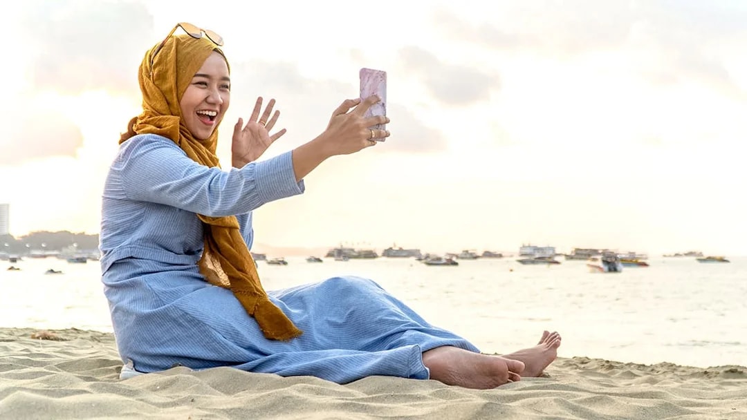 Woman on beach video calling with smartphone, Kuala Lumpur 5G SIM Card.