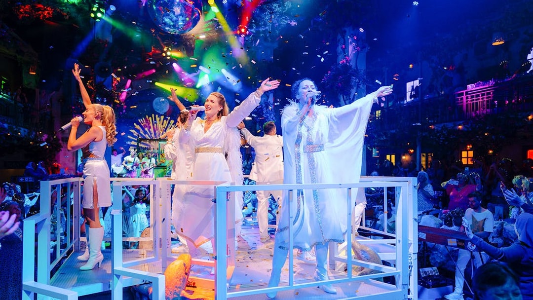 Performers singing on stage at Mamma Mia! The Party with colorful lights and audience.