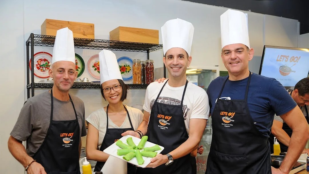 Culinary tour participants in chef hats holding a dish during a cooking class.