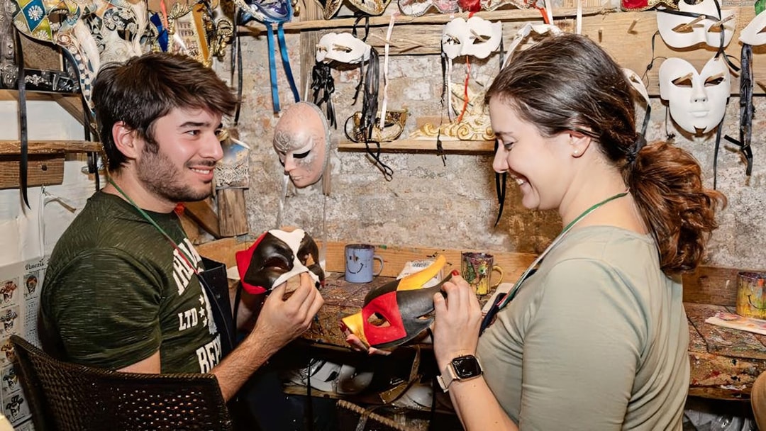 Couple painting masks at a workshop, surrounded by colorful masks and art supplies.