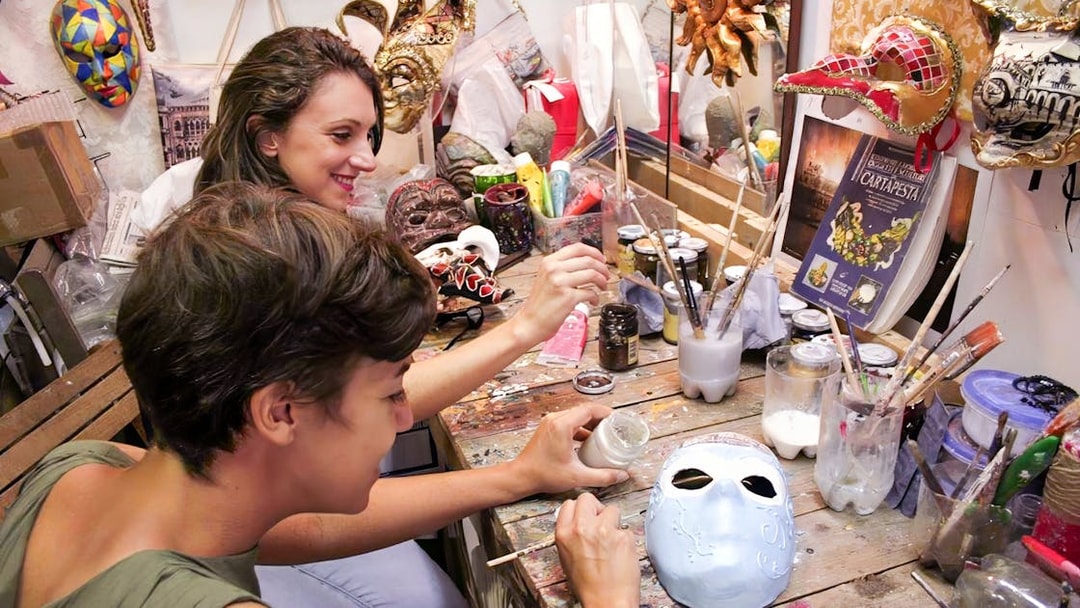 Participants painting masks at a workshop table with various art supplies.