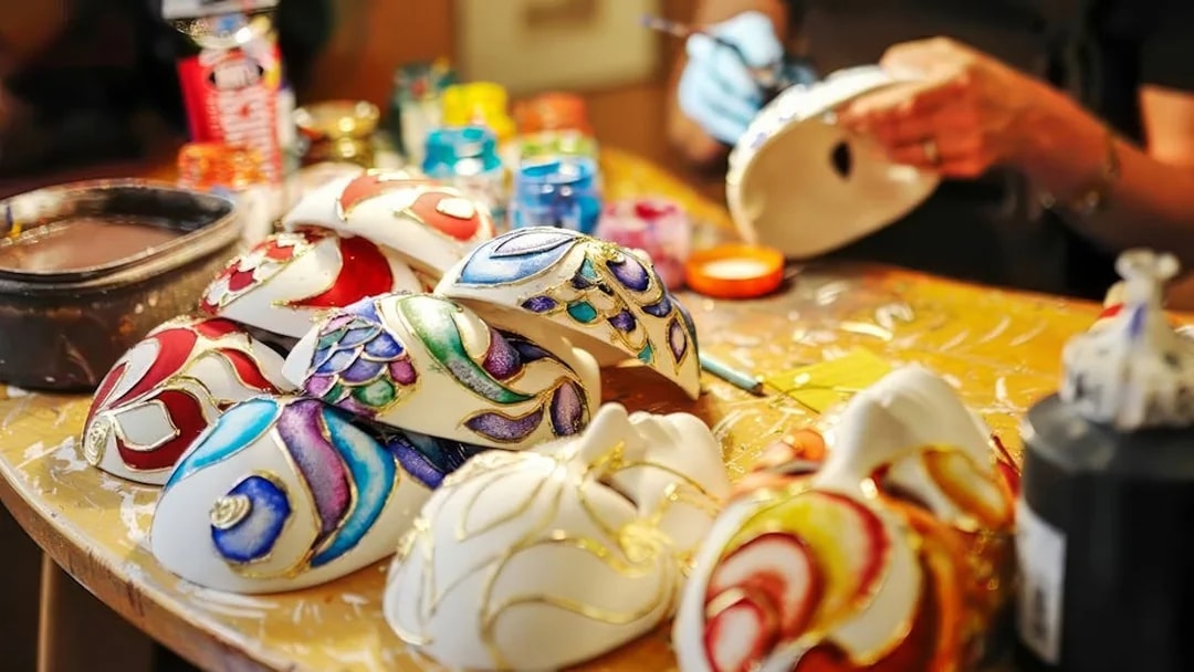 Colorful masks being painted at a workshop table with various paints and brushes.