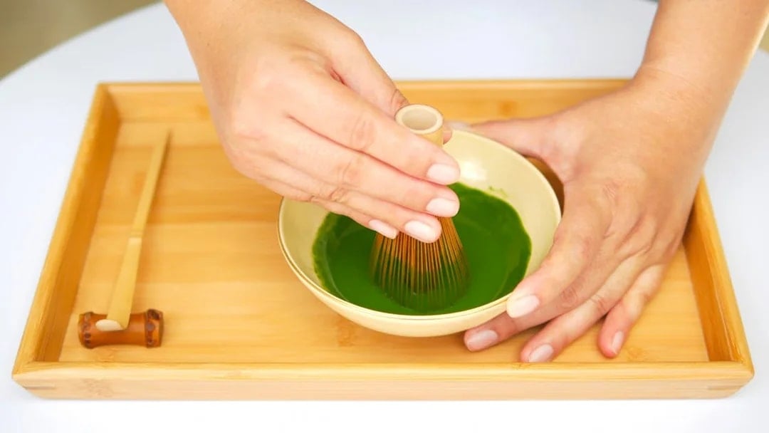 Whisking matcha in a bowl on a bamboo tray.