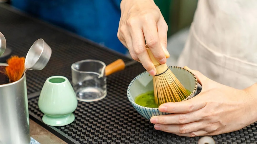 Barista whisking matcha green tea in a bowl.