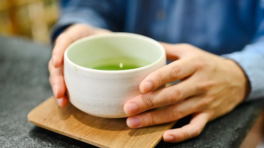 Man holding a bowl of matcha tea on a wooden coaster.