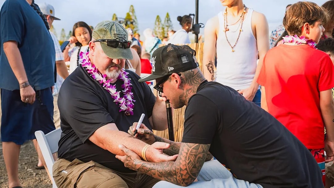 Man receiving traditional Hawaiian tattoo on arm at Mauka Warriors Luau.