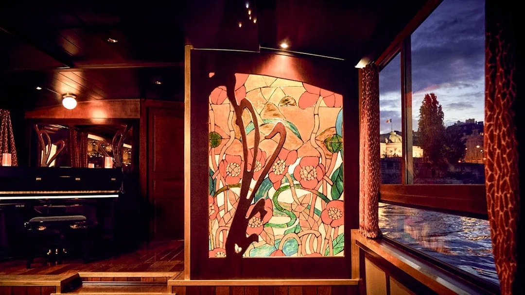 Stained glass art and piano inside Maxim's Seine River cruise boat at sunset.